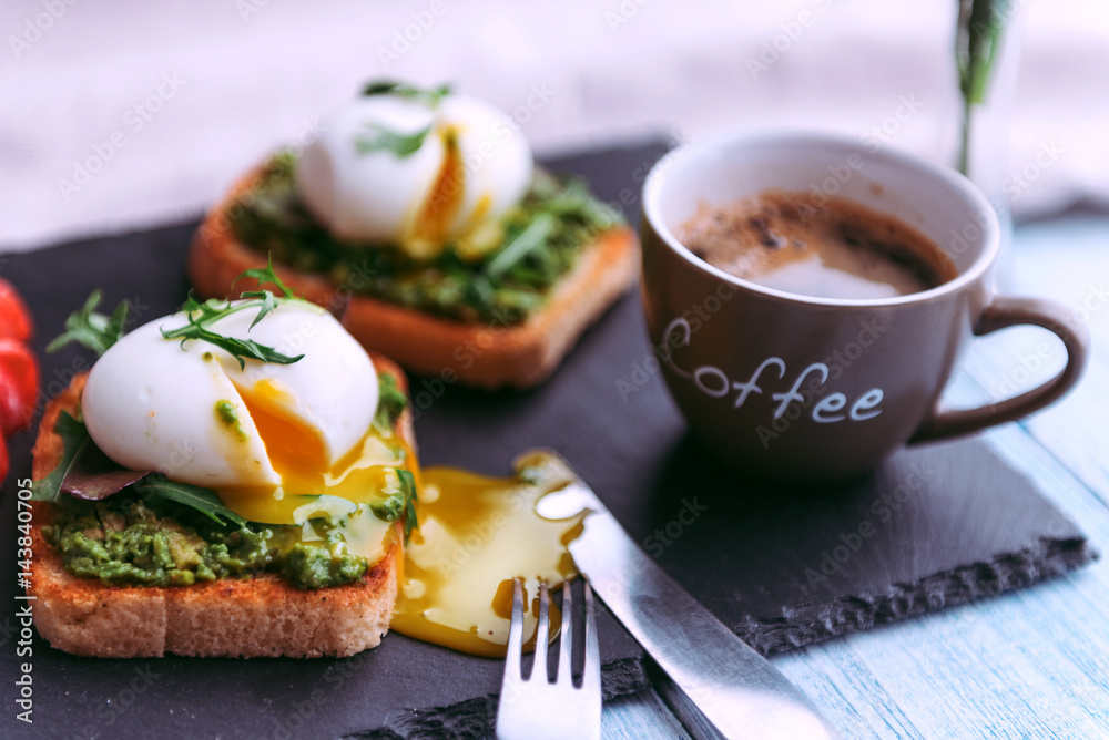 Breakfast with egg poached on avocado paddle and basil and a cup of coffee