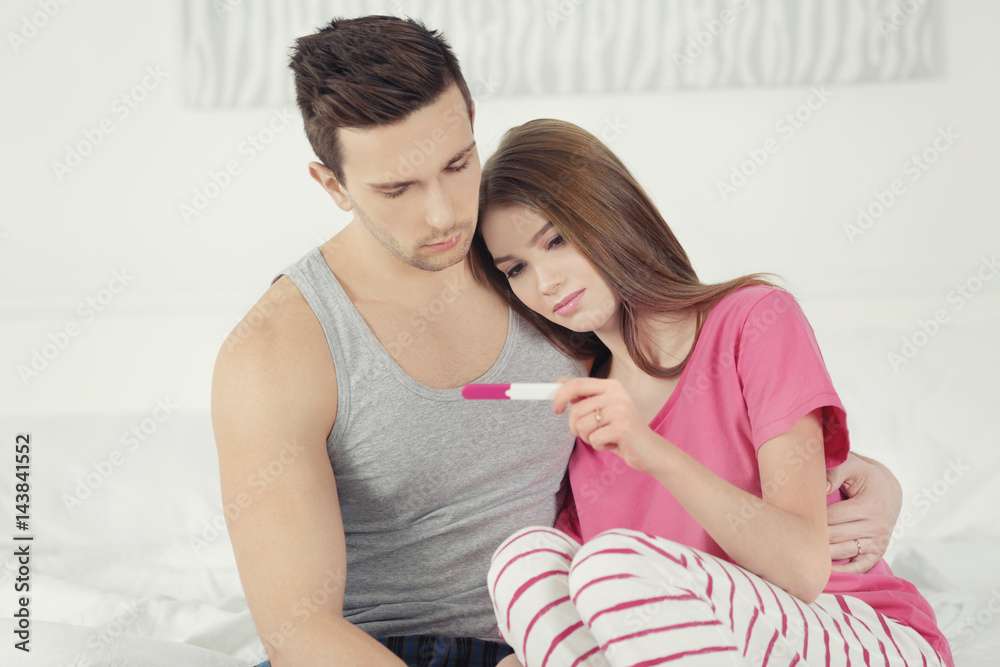 Upset couple sitting on bed and looking at pregnancy test Upset couple sitting on bed and looking at pregnancy test