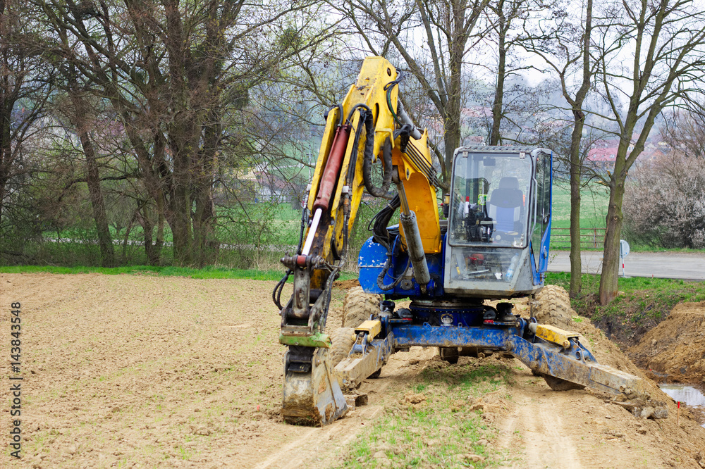excavator in a field, digger ready for digging trough roadside, muddy excavator 
