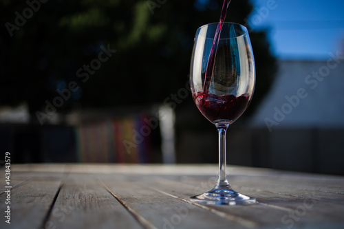 Close up image of wine being poured into a glass on a wooden table outside with natural light