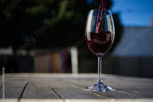 Close up image of wine being poured into a glass on a wooden table outside with natural light