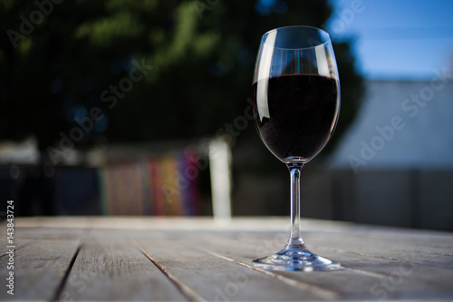 Close up image of wine being poured into a glass on a wooden table outside with natural light