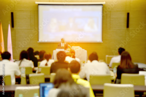 Blurred image of education people, business people and students sitting in large hal with screen and projector for showing information