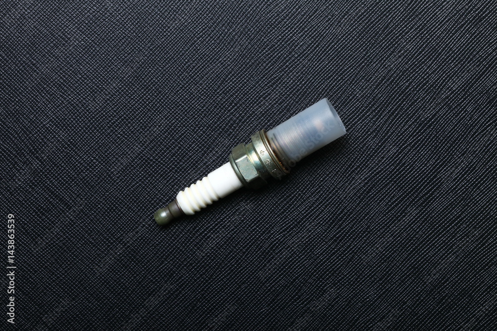 Used and old spark plug after change a new one to engine put on the black color leather surface background represent the worthless car part condition. Used and old spark plug after change a new one to engine put on the black color leather surface background represent the worthless car part condition.