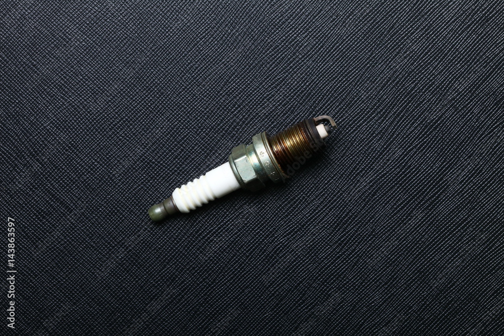 Used and old spark plug after change a new one to engine put on the black color leather surface background  represent the worthless car part condition.
