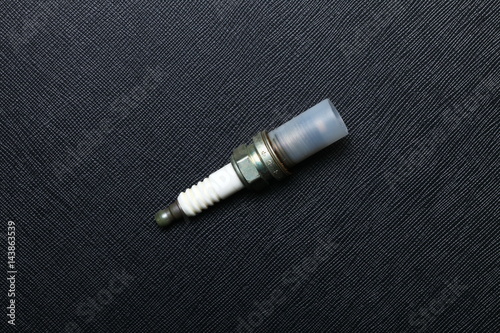 Used and old spark plug after change a new one to engine put on the black color leather surface background represent the worthless car part condition.