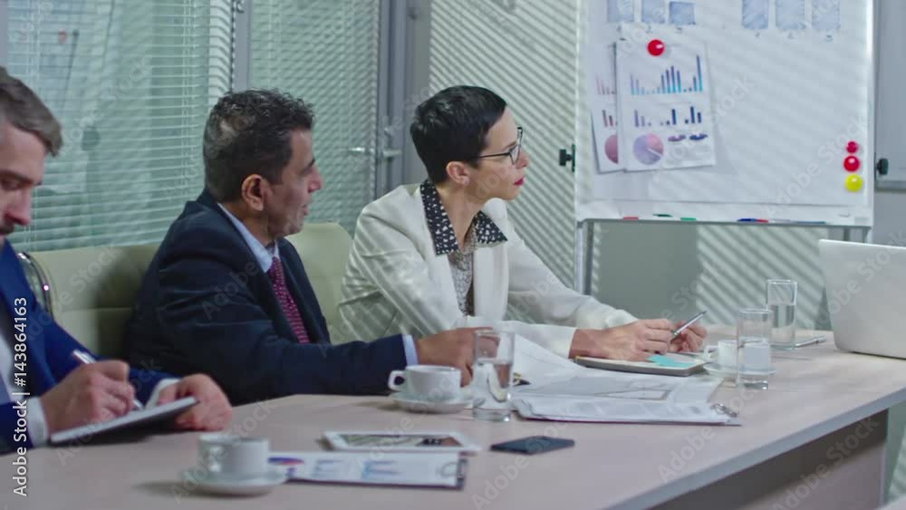 PAN of businesswoman in glasses and bearded employee in suit listening to Arab businessman discussing financial report with female executive during meeting in conference room PAN of businesswoman in glasses and bearded employee in suit listening to Arab businessman discussing financial report with female executive during meeting in conference room
