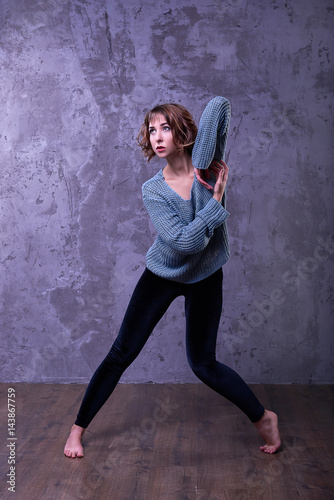 One sexy girl dancer with flowing short brown hair of curls in a gray knitted sweater and black velvet leggings beautiful dancing posing with awesome hands and long thin legs on gray background 