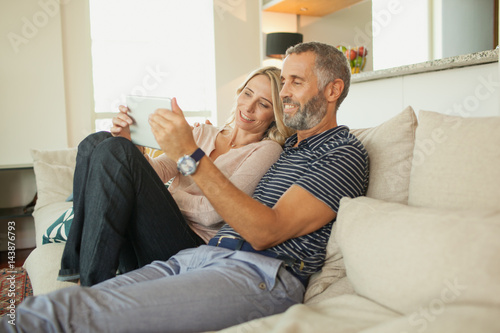 Couple using digital tablet on couch.