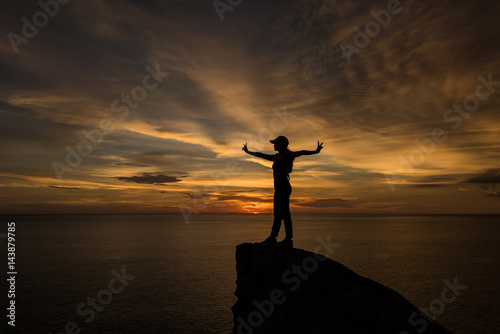 silhouette of woman hand up and standing on rock in sunset. 