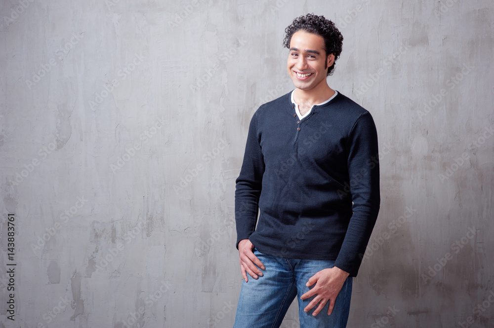 Charming and self-confident. Handsome young arabic man holding hand in pockets and looking at camera while standing against grey background Charming and self-confident. Handsome young arabic man holding hand in pockets and looking at camera while standing against grey background