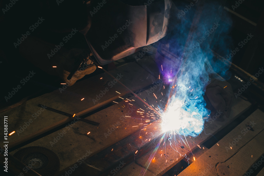 Worker with personal protective equipment and protective mask welding steel pipe in factory.
