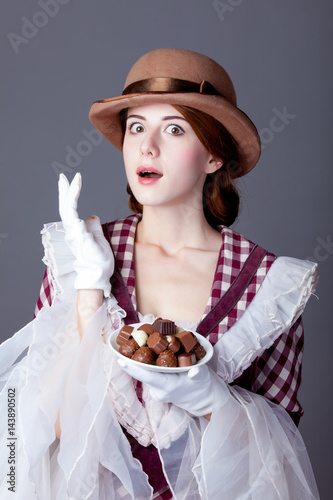 photo of beautiful young woman in vintage dress with plate full of chocolates