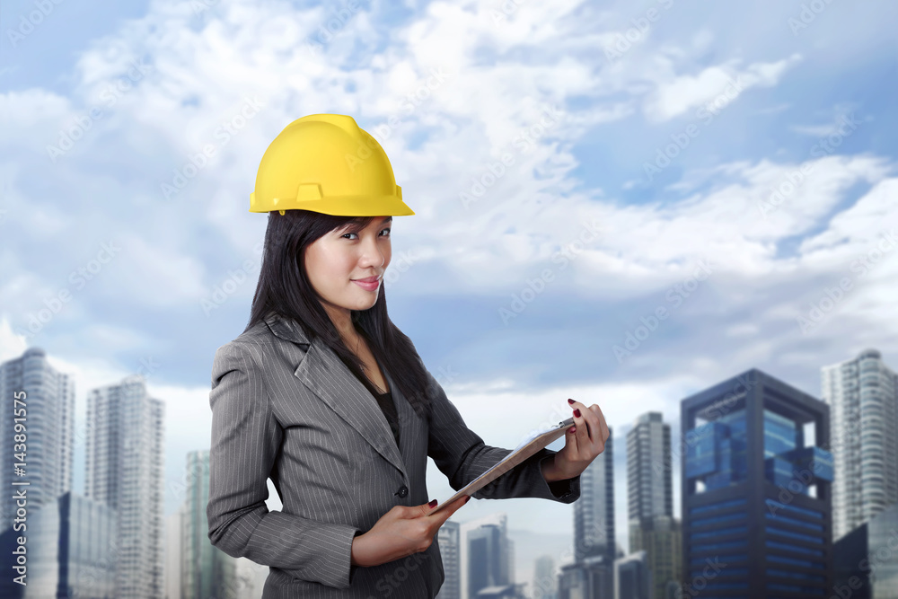 Smiling asian contractor woman with yellow helmet holding clipboard Smiling asian contractor woman with yellow helmet holding clipboard