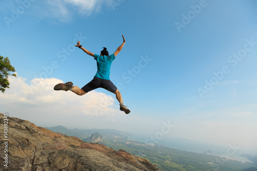 successful woman jumping on rocky mountain peak, freedom, risk, challenge, success concept