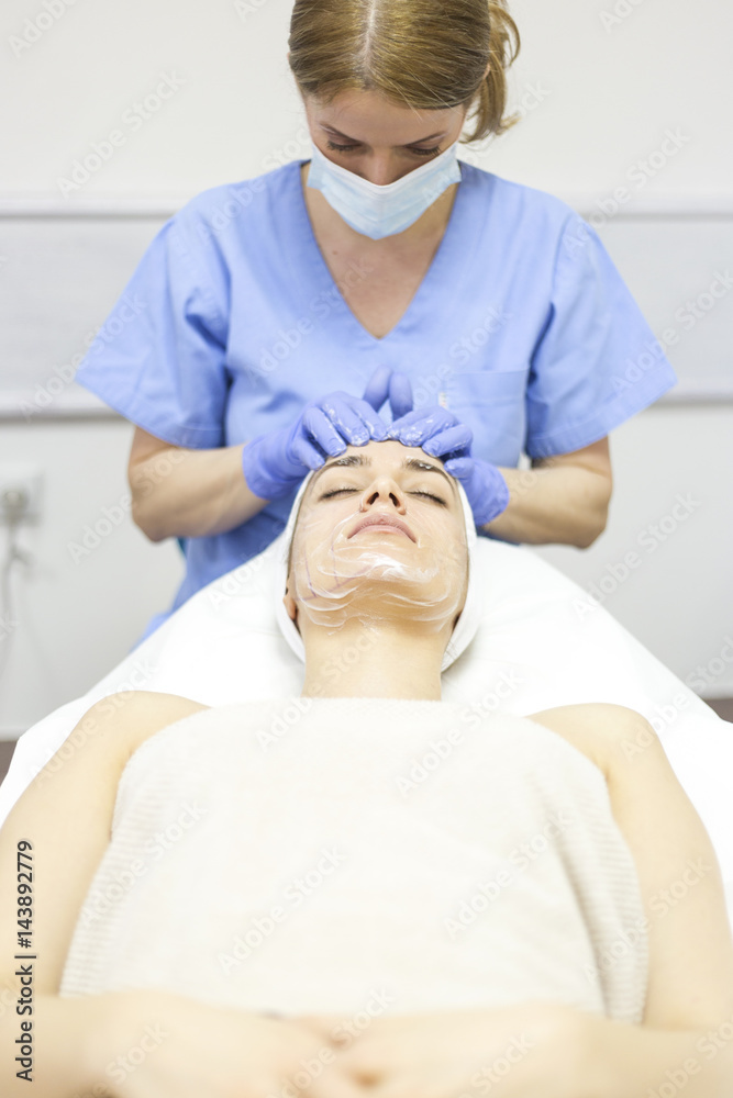 Fototapeta premium Beautiful woman at spa salon, Cosmetician woman applying facial mask.