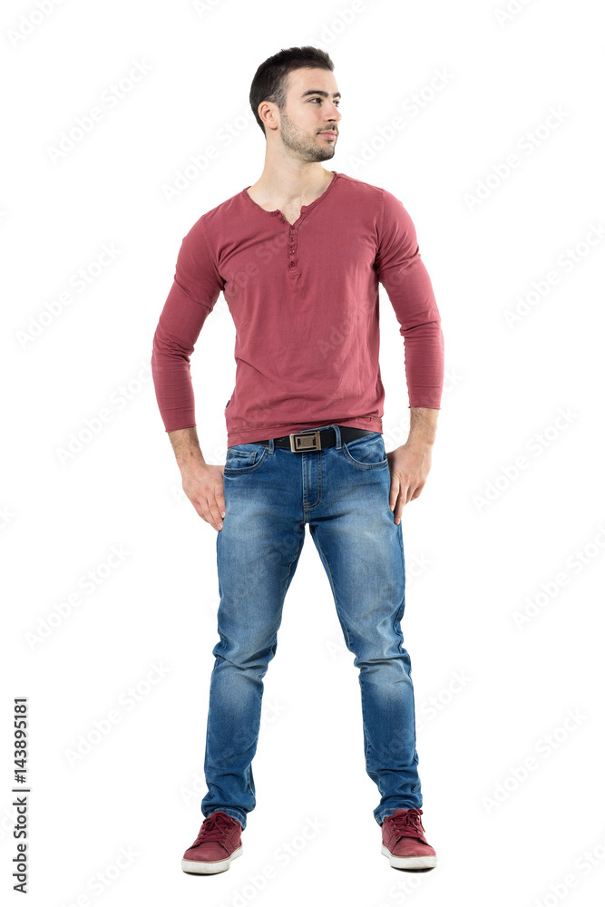 Relaxed young happy stylish man wearing v-neck shirt with hands on hips looking away.  Full body length portrait isolated over white background. 