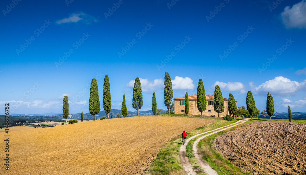 Scenic Tuscany landscape with farmhouse and cyclist on a sunny day, Italy