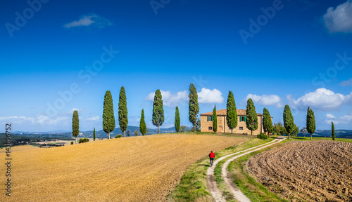 Scenic Tuscany landscape with farmhouse and cyclist on a sunny day, Italy