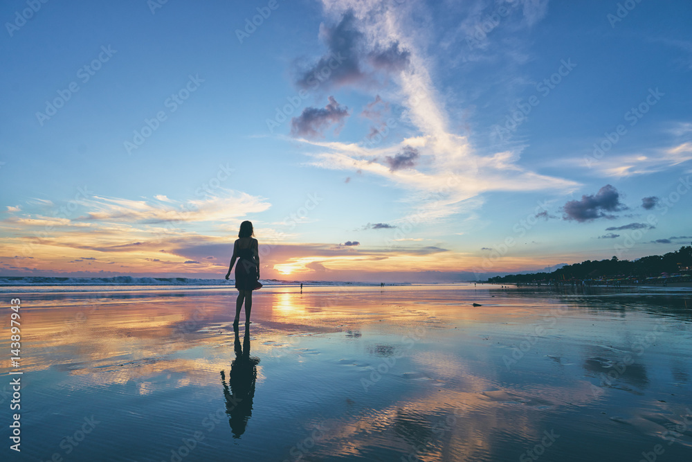 Fototapeta premium Niebo i morze. Piękny zachód słońca. Sylwetka młodej kobiety spaceru na plaży oceanu.