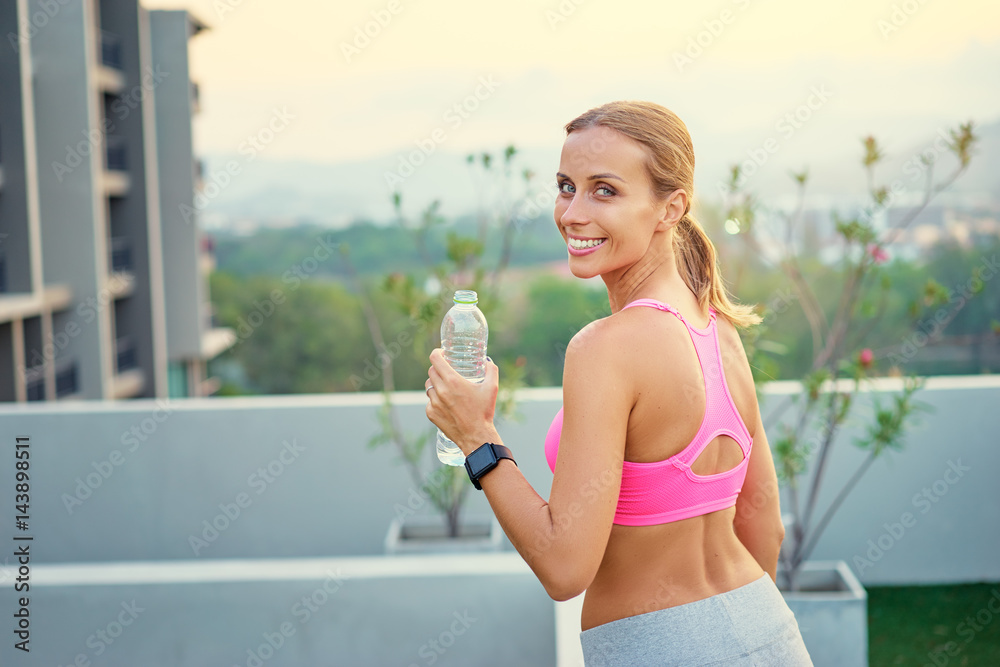 Technology and healthy lifestyle. Pretty young woman in sports wear with smartwatch tracker holding bottle of water outdoors.