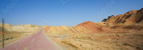 Long empty red brick road in desert with clear blue sky .