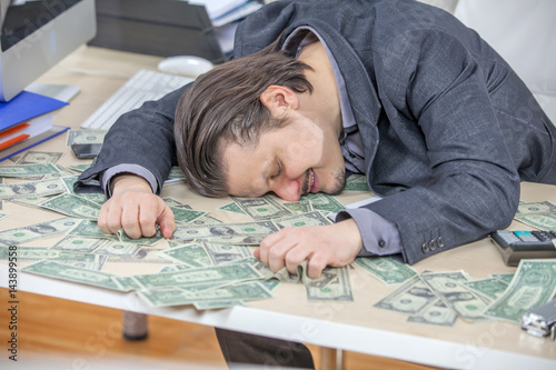 A businessman is hugging all the money on the table in front of him. He is happy.