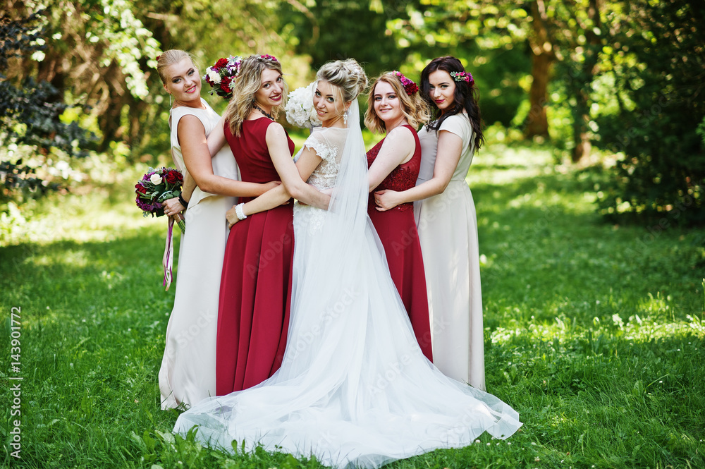 Gorgeous blonde bride with four bridesmaids at red and beige dresses outdoor.