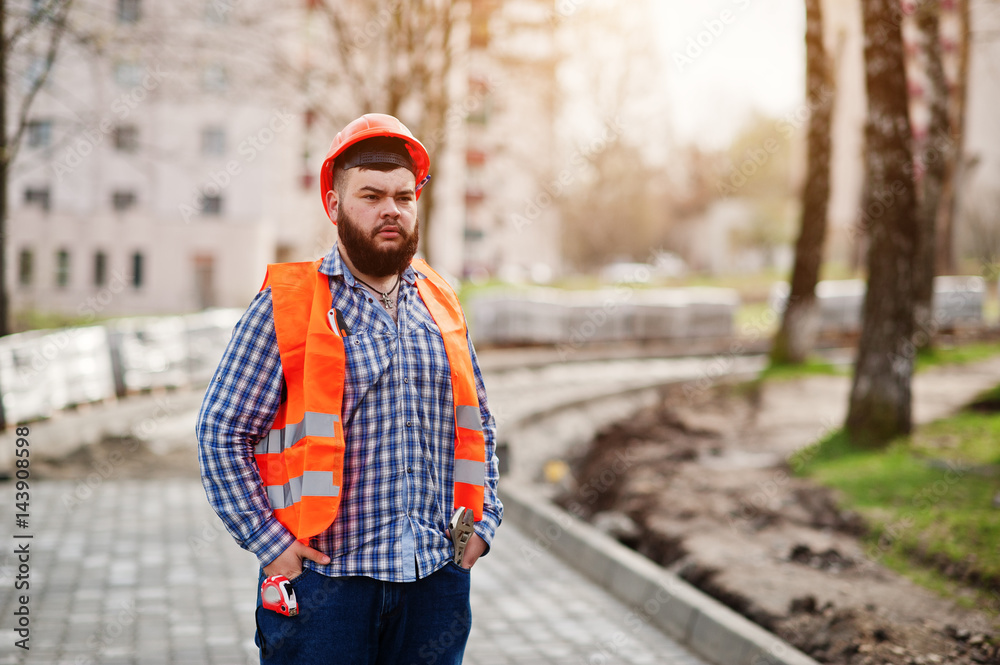 Portrait of brutal beard worker man suit construction worker in safety orange helmet against pavement. Portrait of brutal beard worker man suit construction worker in safety orange helmet against pavement.