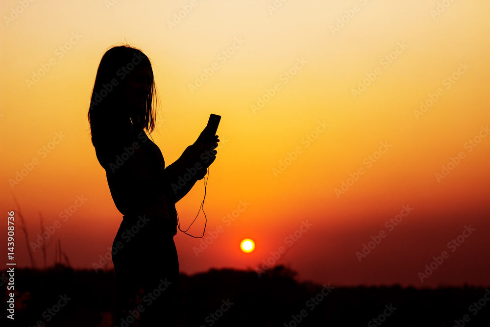 Silhouette woman taking photo of sunset by using smartphone