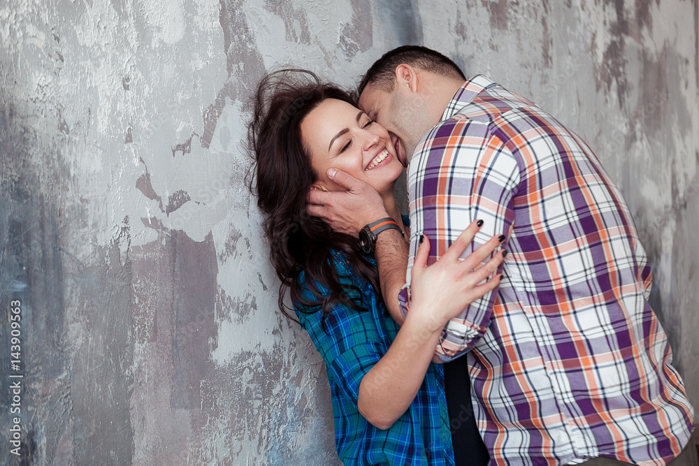 Portrait of beautiful young couple in casual clothes hugging and smiling, standing against gray wall