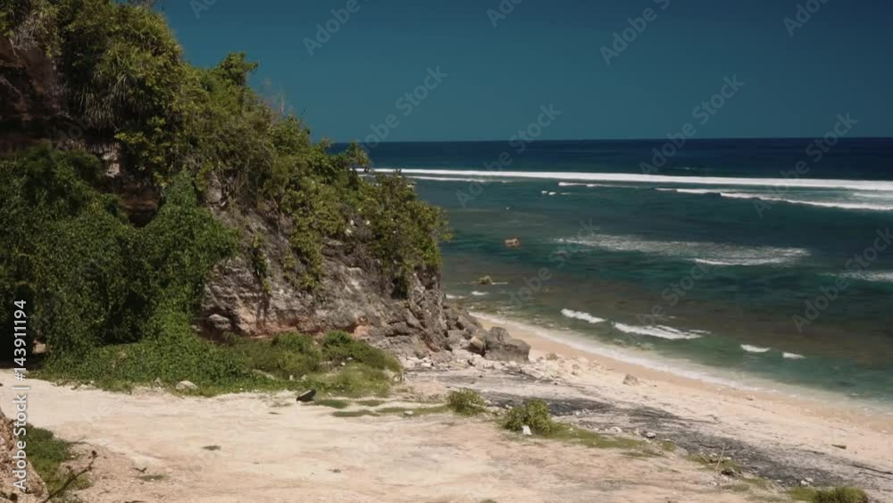 Empty white beach bordered by rocks with trees and vines on sunny summer day in south Bali. Shot with Sony a7s on slider