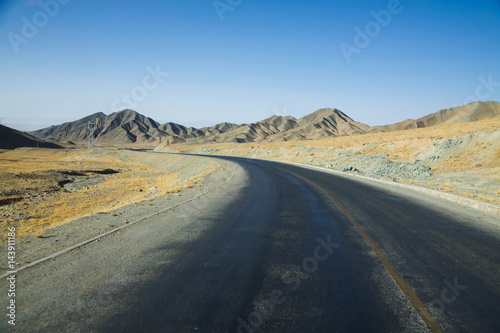Long empty curve asphalt road in desert with clear blue sky .