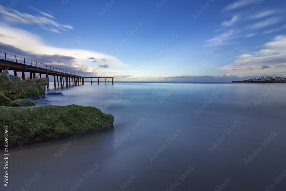 tranquility and calm sea with bridge and stones with algae .