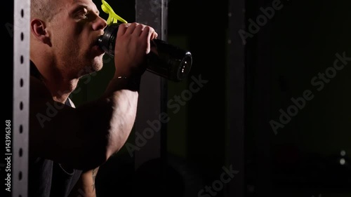 Young tired bodybuilder in a gym drinking from a shaker. 60 to 24fps 4K