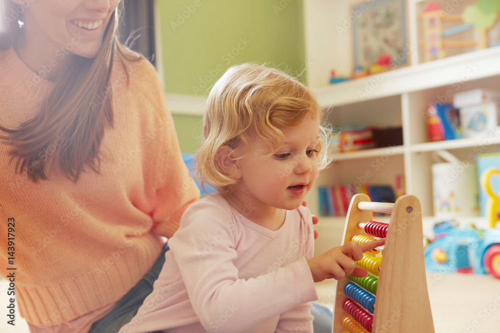 Mid adult woman and toddler daughter counting on abacus in playroom Mid adult woman and toddler daughter counting on abacus in playroom
