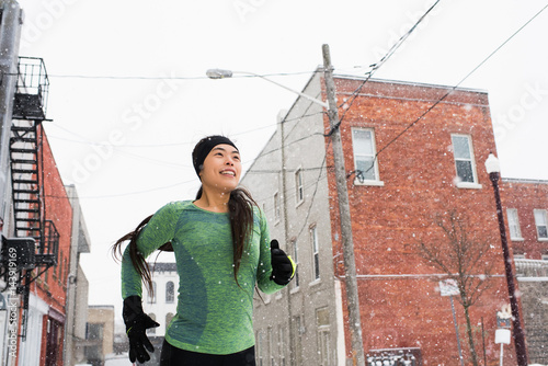 Happy young female runner in knit hat running in snowy street photo