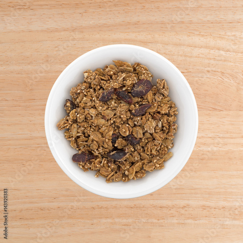 Organic cranberry nut granola in a small white bowl atop a wood table top.