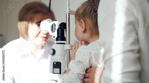 Little adorable girl in child's ophthalmology - optometrist checking eyesight photo