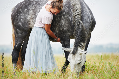 Woman in skirt with arms around dapple grey horse in field