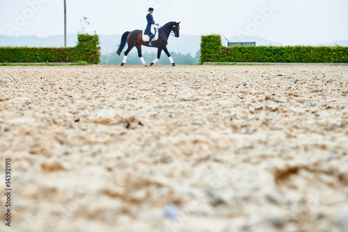 Distant view of rider trotting while training dressage horse in equestrian arena
