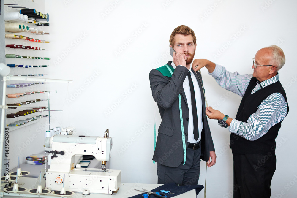 Fotografie Young businessman speaking on cellphone while visiting tailor