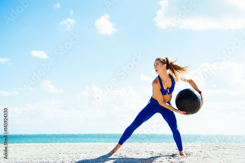 Young woman training, preparing to throw exercise ball on beach photo