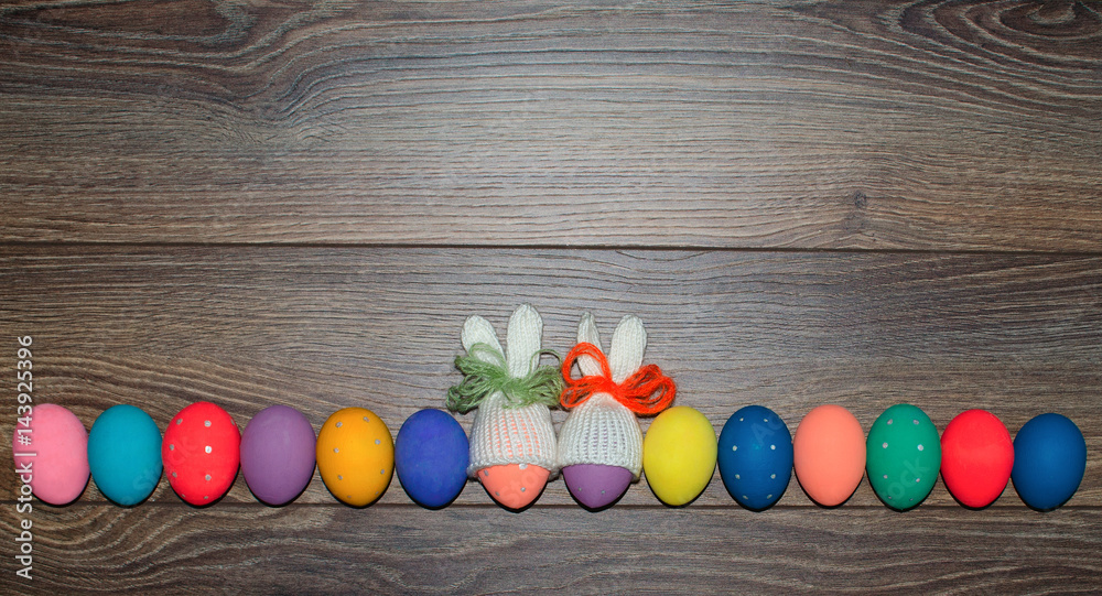 Obraz premium Easter eggs hand painted with knitted bunny hats over wooden background with copy space . Happy Easter