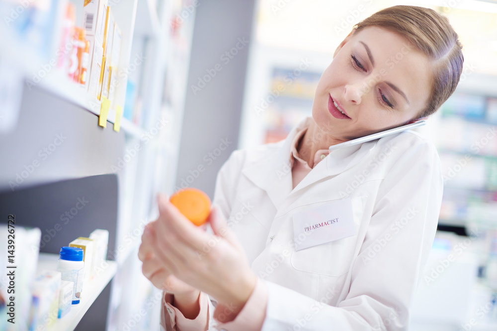 Female pharmacist on phone call reaching medication . Female pharmacist on phone call reaching medication .