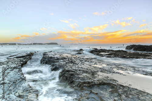 Surfers at Currumbin Rock Gold Coast at sunset, with ocean current rushing against a large rock