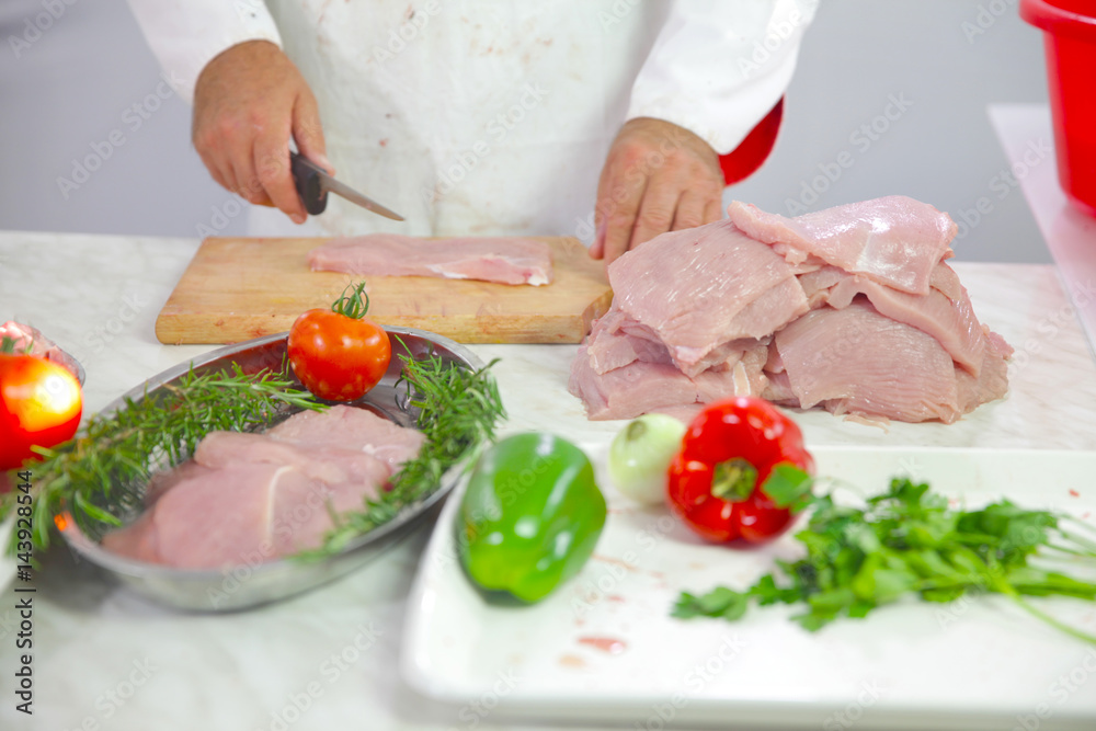 A chef is nicely cutting and putting pieces of turkey meat on a tray together with fresh vegetables. He will put everything into the oven.