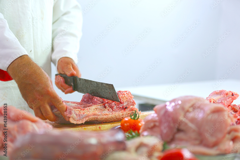 Butcher is cutting meat at his job. He is holding a big knife in his hands.