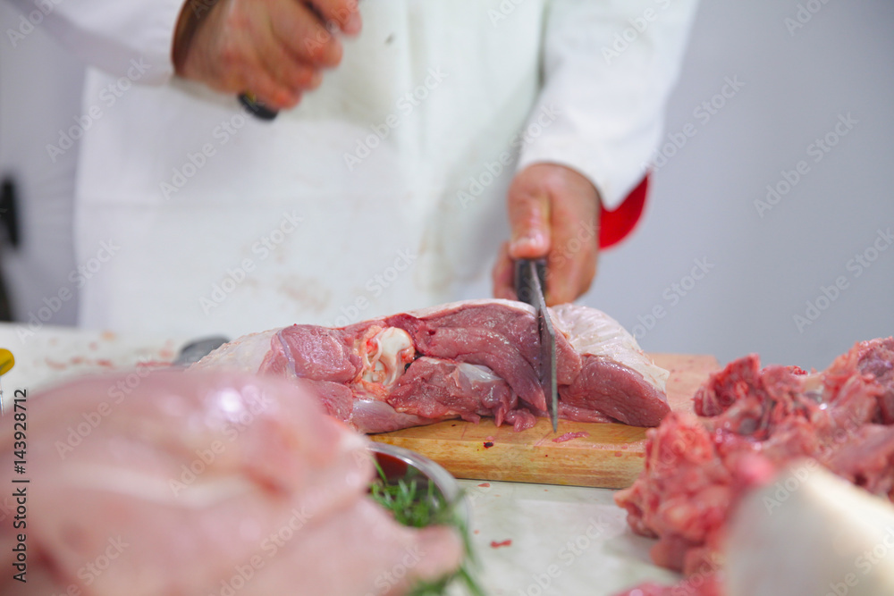 A middle-aged chef is cutting red meat with a big knife. 