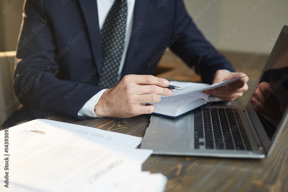 Closeup portrait of unrecognizable successful businessman analyzing contract documents at desk with laptop Closeup portrait of unrecognizable successful businessman analyzing contract documents at desk with laptop